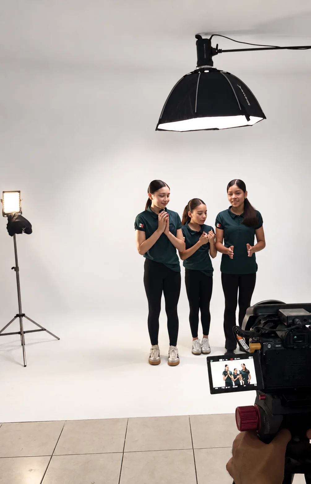 Tres mujeres durante una grabación en el ciclorama blanco, con cámara y luz de estudio en primer plano.