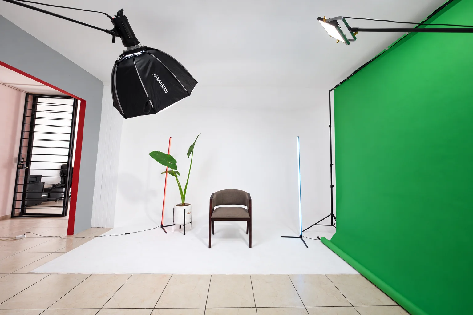 Vista amplia real del estudio: ciclorama blanco, silla, planta, iluminación y croma verde; luz y color retocados con IA desde DSC04030.