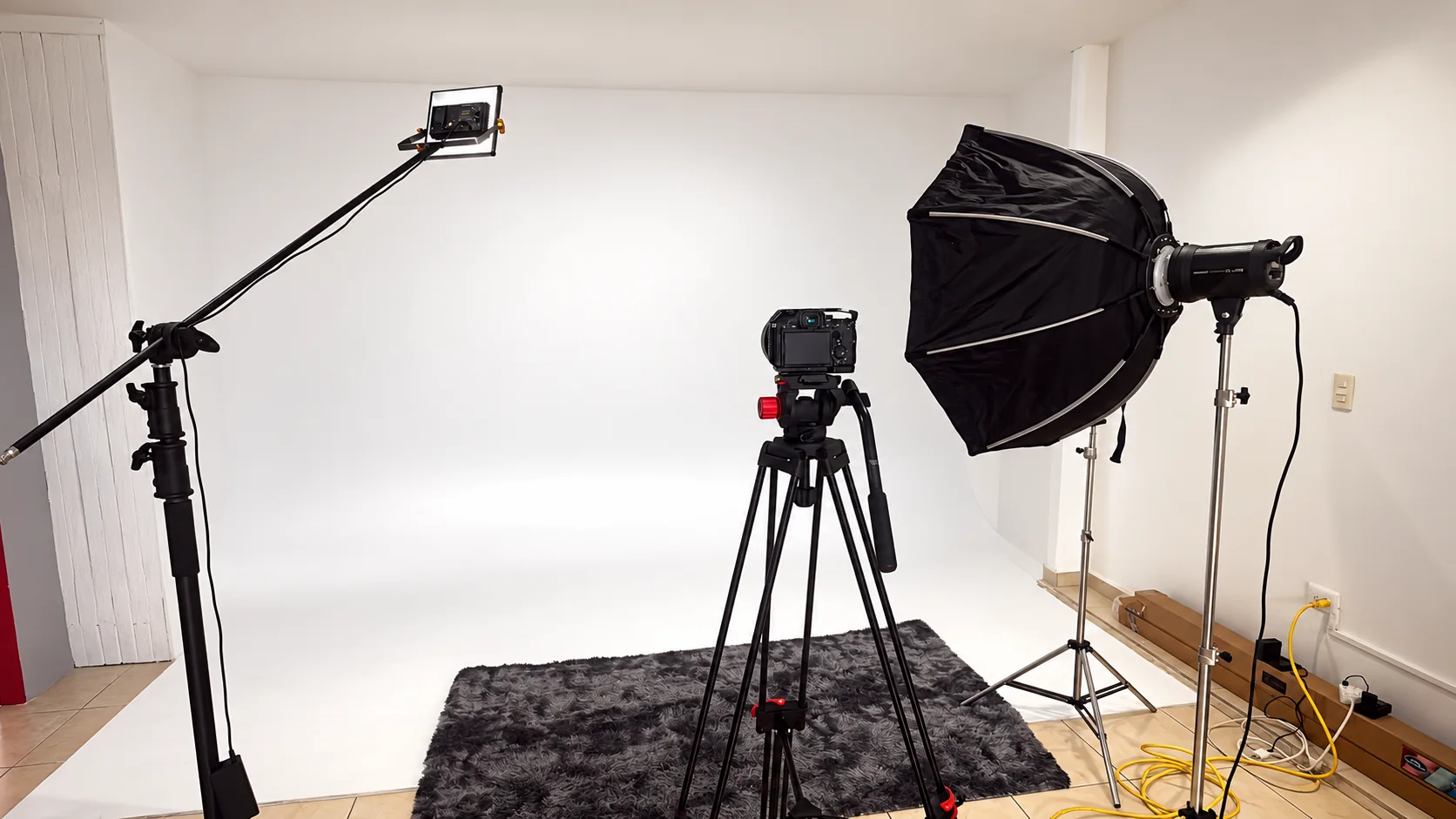 Cámara sobre tripié y softbox frente al ciclorama blanco, listos para una producción de video.